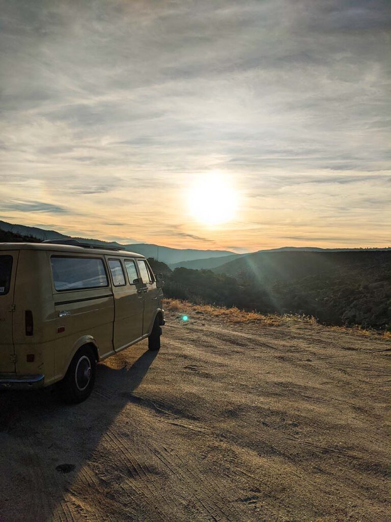 A classic camper van parked at sunset with a scenic mountain view, representing the peace of mind and off-grid freedom that comes with Vanpire Customs' professional RV membership services in Los Angeles, California.
