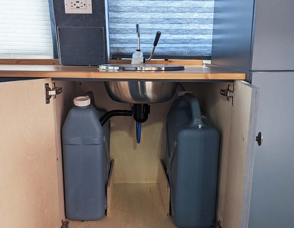 Expertly installed camper van plumbing system by Vanpire Vans, featuring organized fresh and grey water tanks under the sink for efficient off-grid living