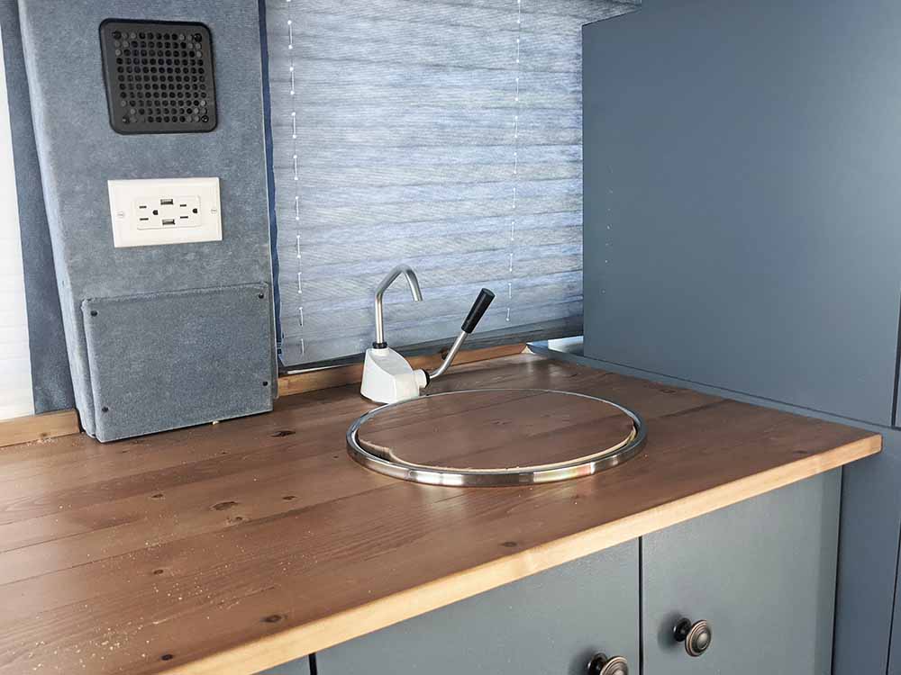 Close-up of a custom camper van kitchen area featuring a wooden countertop, sink, and electrical outlets, expertly crafted by Vanpire Vans for off-grid travel
