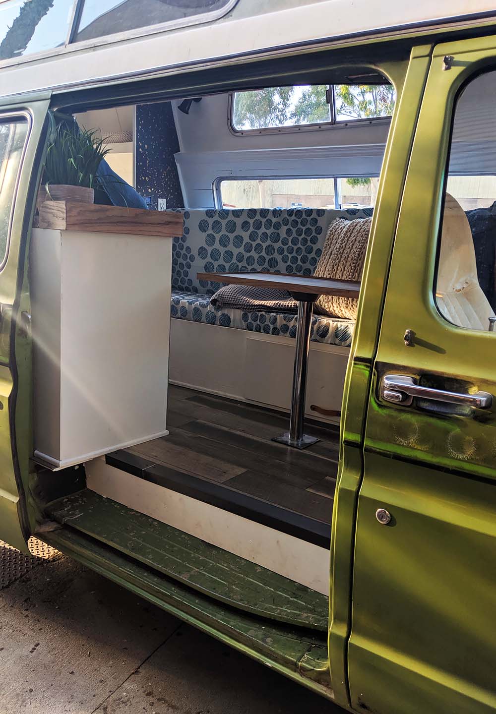 Detailed view of a custom camper van interior built by Vanpire Vans in Los Angeles, featuring wood flooring, kitchenette, and patterned seating.